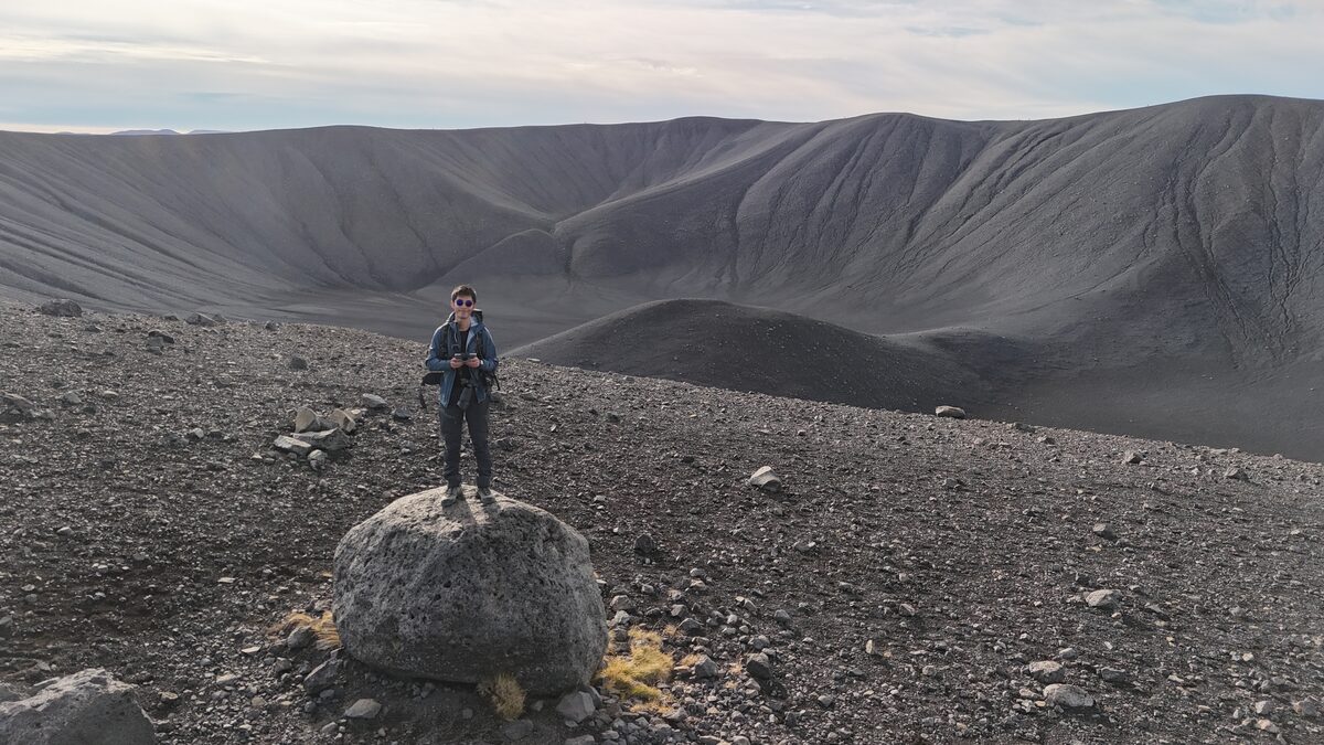 TY on a rock inside Hverfjall crater, Iceland — drone frame showing crater scale